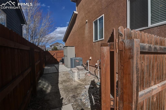 view of side of home featuring central AC, a fenced backyard, and stucco siding