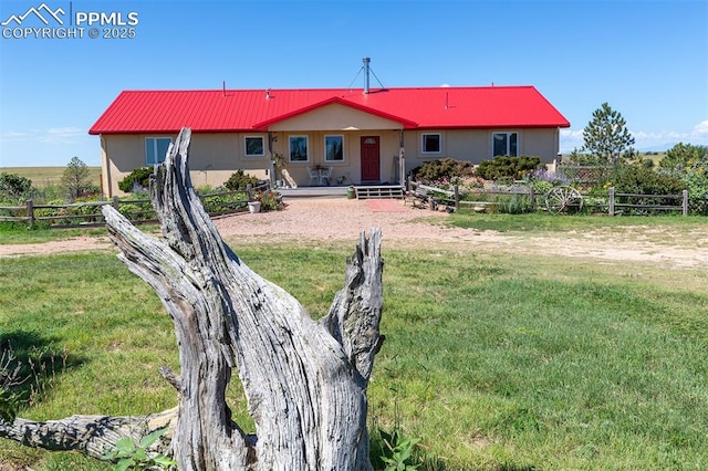 back of house featuring a yard, metal roof, fence, and stucco siding