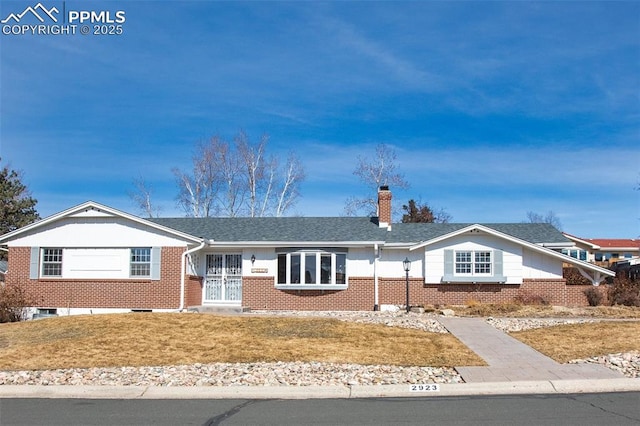 ranch-style home with a front yard, brick siding, a chimney, and roof with shingles