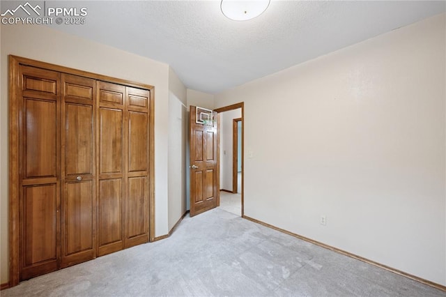 unfurnished bedroom with light carpet, a textured ceiling, a closet, and baseboards