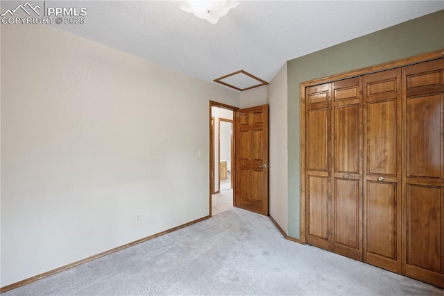 unfurnished bedroom with baseboards, a closet, attic access, and light colored carpet