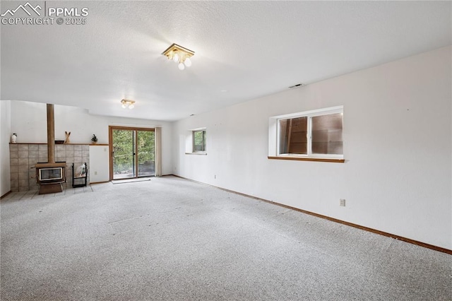 unfurnished living room with a textured ceiling, carpet flooring, visible vents, baseboards, and a wood stove