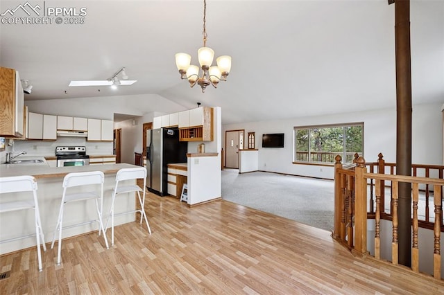 kitchen featuring stainless steel appliances, a sink, vaulted ceiling, a peninsula, and under cabinet range hood