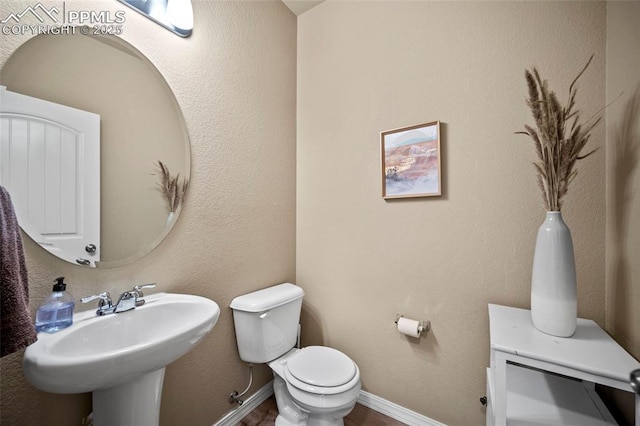 bathroom with wood finished floors, baseboards, a sink, toilet, and a textured wall