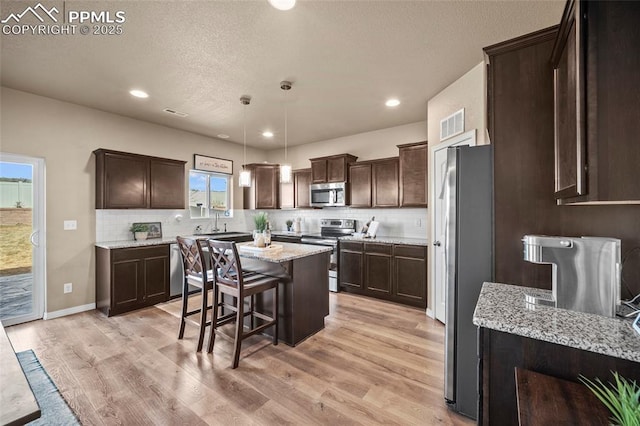 kitchen featuring a center island, appliances with stainless steel finishes, light wood finished floors, decorative backsplash, and dark brown cabinets