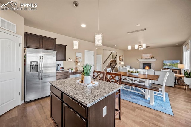 kitchen featuring visible vents, stainless steel fridge with ice dispenser, dark brown cabinets, a glass covered fireplace, and a kitchen breakfast bar