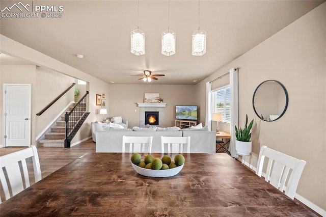 dining space featuring baseboards, stairs, wood finished floors, a glass covered fireplace, and a ceiling fan