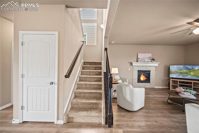 stairway with a tile fireplace, baseboards, a ceiling fan, and wood finished floors