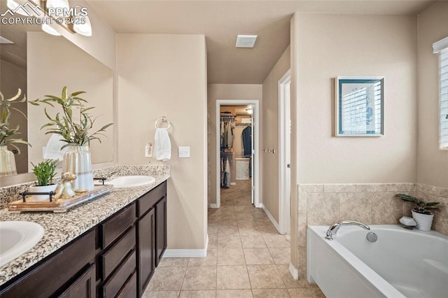 bathroom with a walk in closet, double vanity, a bath, tile patterned floors, and a sink