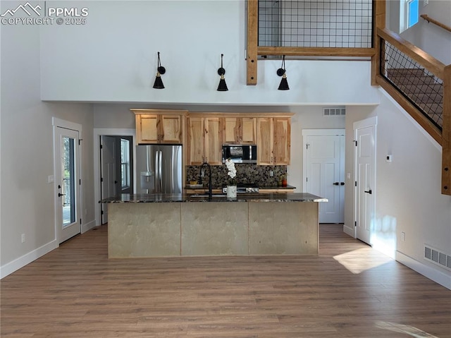 kitchen with dark stone countertops, visible vents, stainless steel refrigerator with ice dispenser, and a towering ceiling