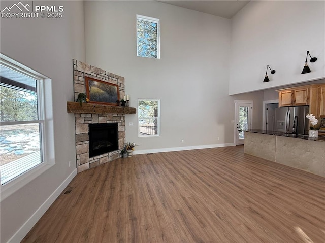 unfurnished living room with a fireplace, wood finished floors, a towering ceiling, and baseboards