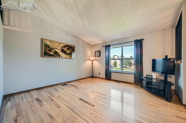 unfurnished living room featuring vaulted ceiling, a textured ceiling, light wood-style flooring, and baseboards