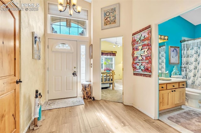 entryway featuring a chandelier, light wood finished floors, a towering ceiling, and baseboards