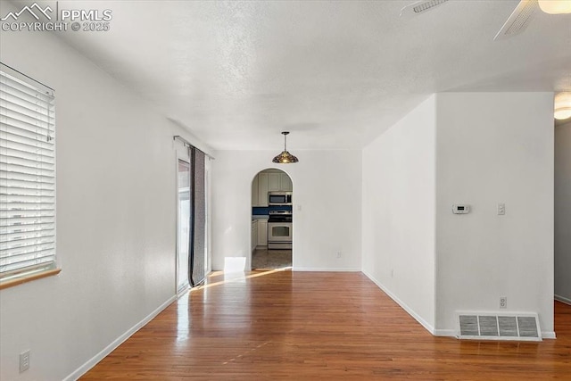 empty room with arched walkways, wood finished floors, a ceiling fan, visible vents, and baseboards