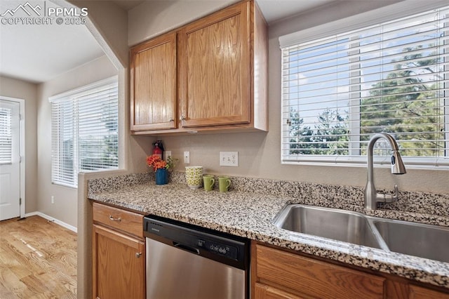 kitchen featuring light stone counters, light wood-type flooring, a sink, and stainless steel dishwasher