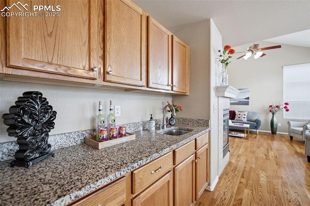 kitchen featuring a ceiling fan, lofted ceiling, light wood-style flooring, light stone counters, and a sink