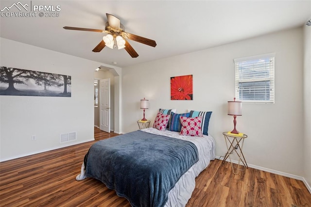 bedroom with arched walkways, ceiling fan, wood finished floors, visible vents, and baseboards