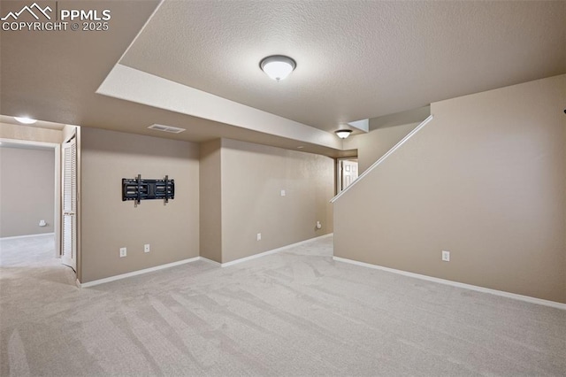 finished below grade area with a textured ceiling, stairway, carpet, and baseboards