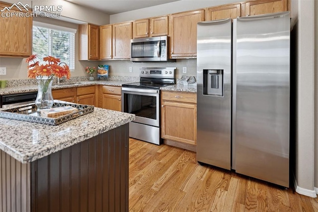 kitchen with stainless steel appliances, light stone countertops, and light wood-style floors