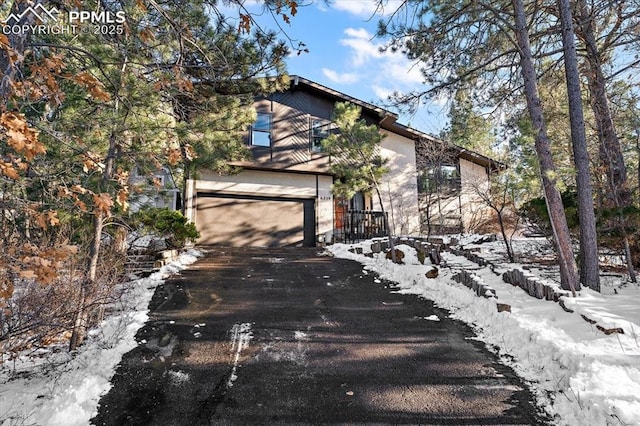 snow covered property featuring a garage and aphalt driveway