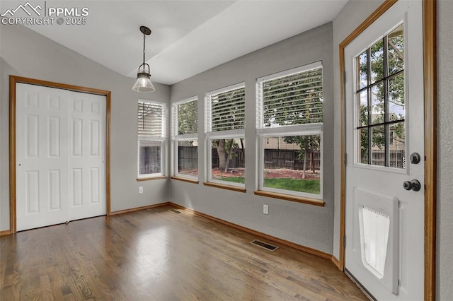 interior space featuring a healthy amount of sunlight, visible vents, vaulted ceiling, and wood finished floors