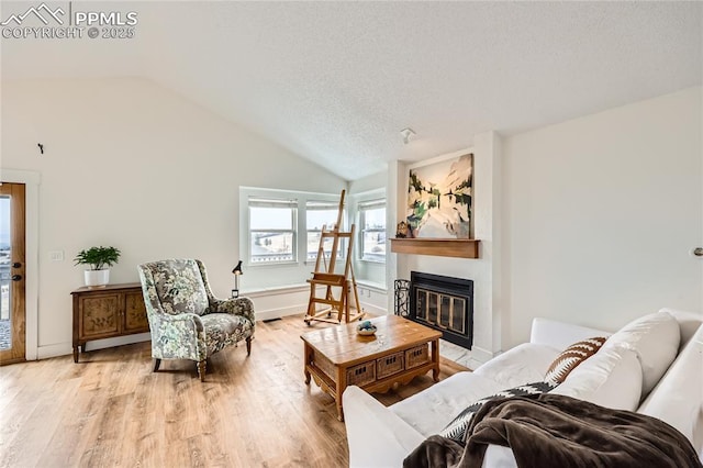 living area featuring light wood-type flooring, lofted ceiling, a glass covered fireplace, and a textured ceiling