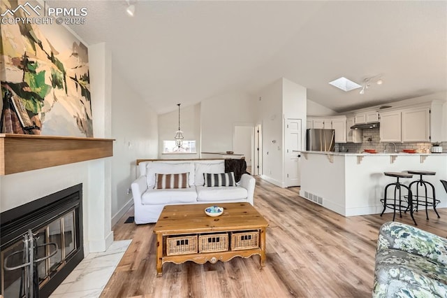 living area featuring vaulted ceiling with skylight, a fireplace with flush hearth, visible vents, and light wood-style floors