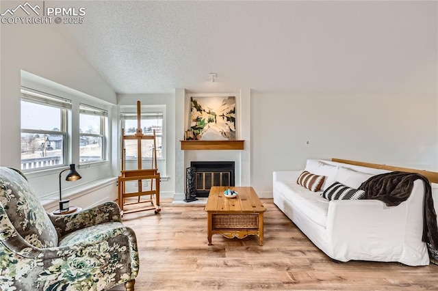 living area with a textured ceiling, a fireplace, wood finished floors, baseboards, and vaulted ceiling