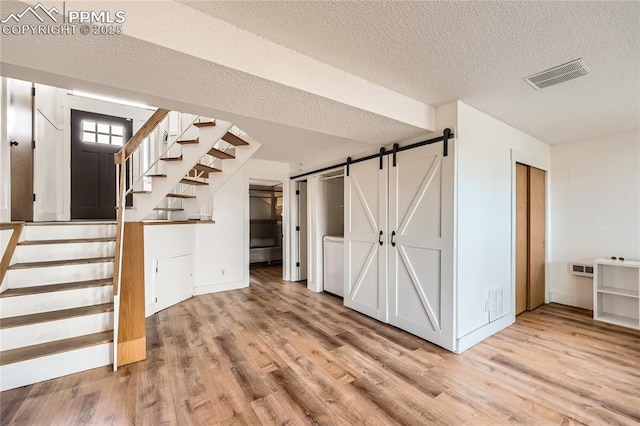 interior space with light wood finished floors, a barn door, visible vents, stairs, and a textured ceiling