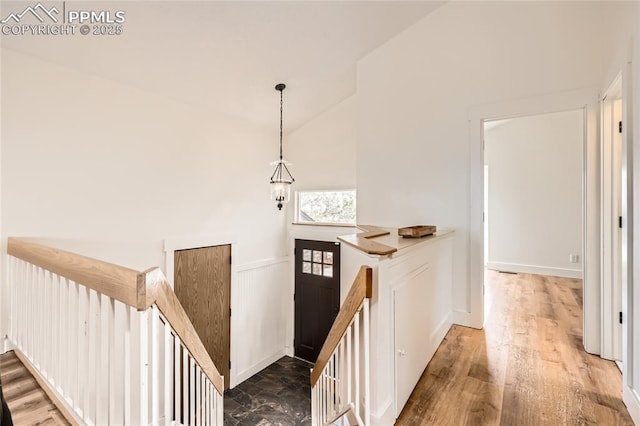 hallway featuring high vaulted ceiling, wainscoting, dark wood finished floors, and an upstairs landing