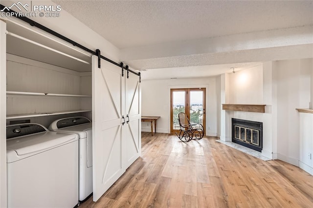 washroom with light wood-style flooring, a barn door, a textured ceiling, laundry area, and independent washer and dryer