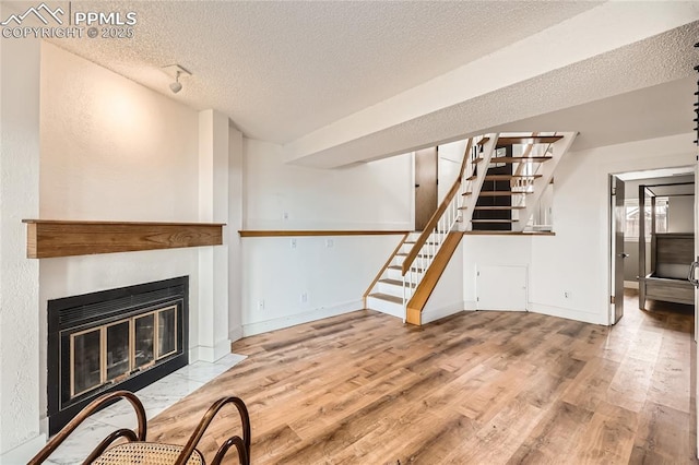 living area featuring a textured ceiling, a fireplace with flush hearth, stairs, and wood finished floors