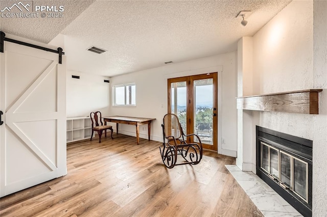 sitting room with a textured ceiling, a barn door, a fireplace, visible vents, and light wood-style floors