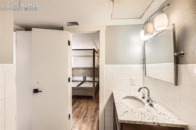 bathroom featuring tile walls, wainscoting, vanity, a textured ceiling, and wood finished floors