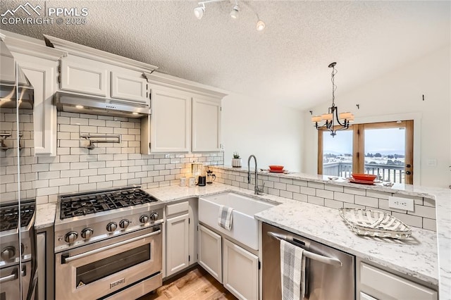 kitchen with lofted ceiling, appliances with stainless steel finishes, under cabinet range hood, white cabinetry, and a sink