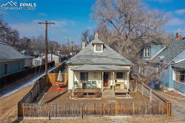 view of front of house with a fenced front yard, covered porch, a shingled roof, and a chimney