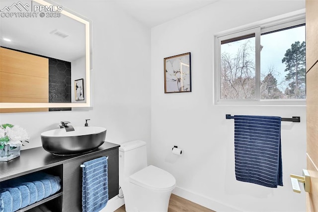 bathroom featuring toilet, baseboards, wood finished floors, and vanity