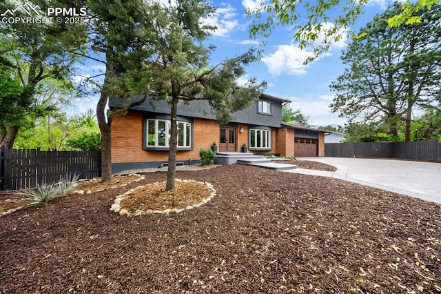 view of front of property featuring brick siding, driveway, an attached garage, and fence