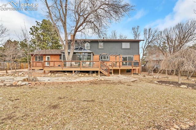 back of property with brick siding, a lawn, a wooden deck, and fence