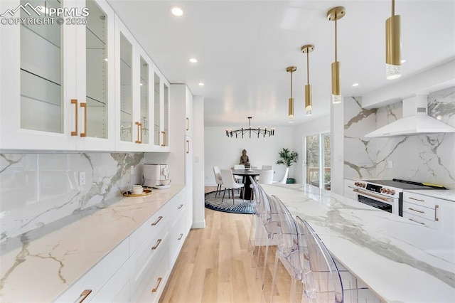 kitchen featuring decorative light fixtures, white cabinets, high end range, glass insert cabinets, and custom range hood