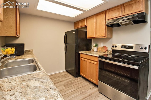 kitchen with brown cabinets, light wood finished floors, a sink, under cabinet range hood, and black appliances