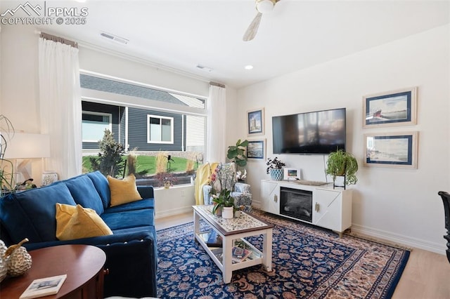 living area with ceiling fan, wood finished floors, visible vents, and baseboards