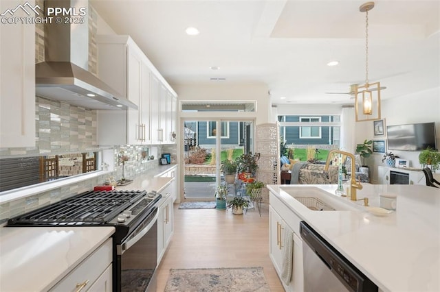 kitchen featuring appliances with stainless steel finishes, light countertops, wall chimney range hood, and white cabinetry