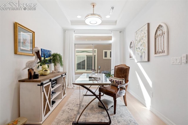 home office featuring a tray ceiling, light wood-style floors, and baseboards