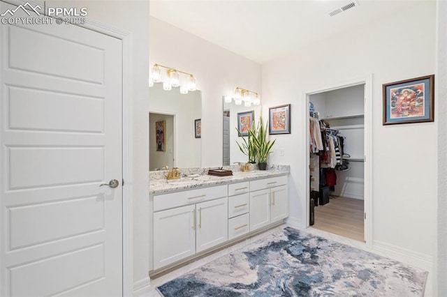 full bath with a walk in closet, visible vents, vanity, and baseboards