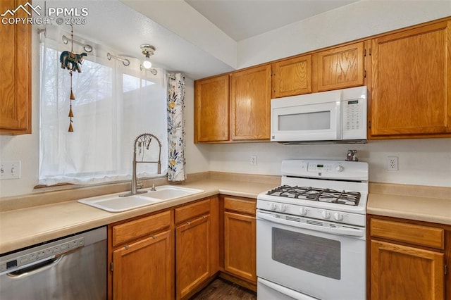 kitchen with light countertops, white appliances, brown cabinetry, and a sink