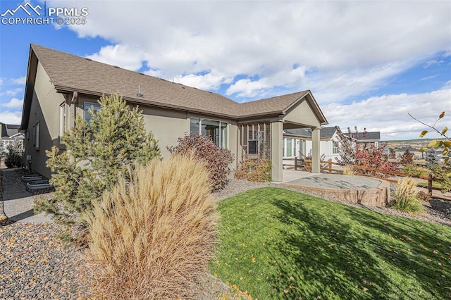 back of property featuring roof with shingles, a lawn, and stucco siding