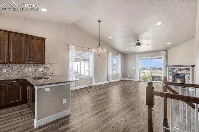 kitchen with stone countertops, open floor plan, vaulted ceiling, a stone fireplace, and a sink