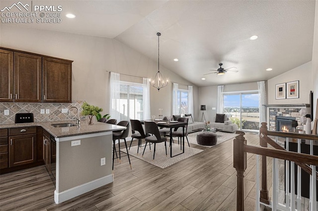 kitchen with lofted ceiling, open floor plan, a peninsula, stone counters, and a sink