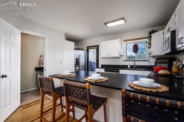 kitchen featuring a sink, white cabinetry, appliances with stainless steel finishes, dark countertops, and a kitchen bar